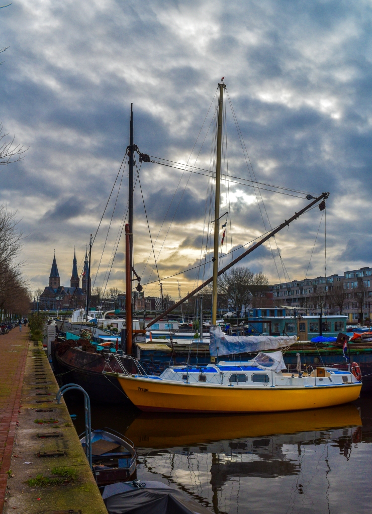 A yellow sailboat anchored at Westerdok in Amsterdam makes a nice subject featuring the Posthoornkerk the background.